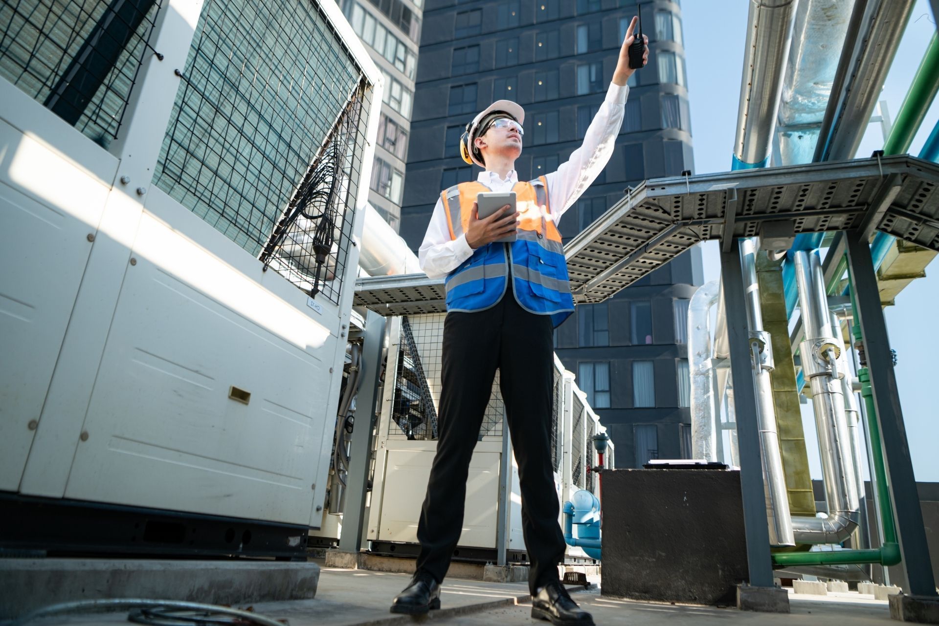 HVAC technician wearing mask and hard hat, working on AC units on a rooftop.