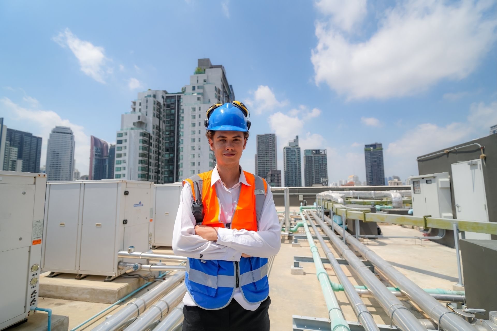 HVAC technician wearing mask and hard hat, working on AC units on a rooftop.