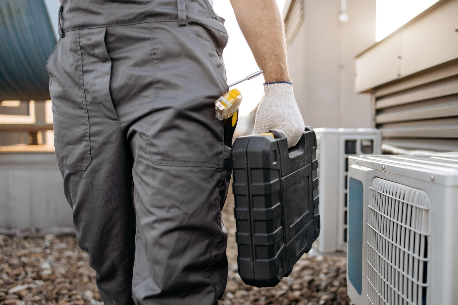 HVAC technician wearing mask and hard hat, working on AC units on a rooftop.