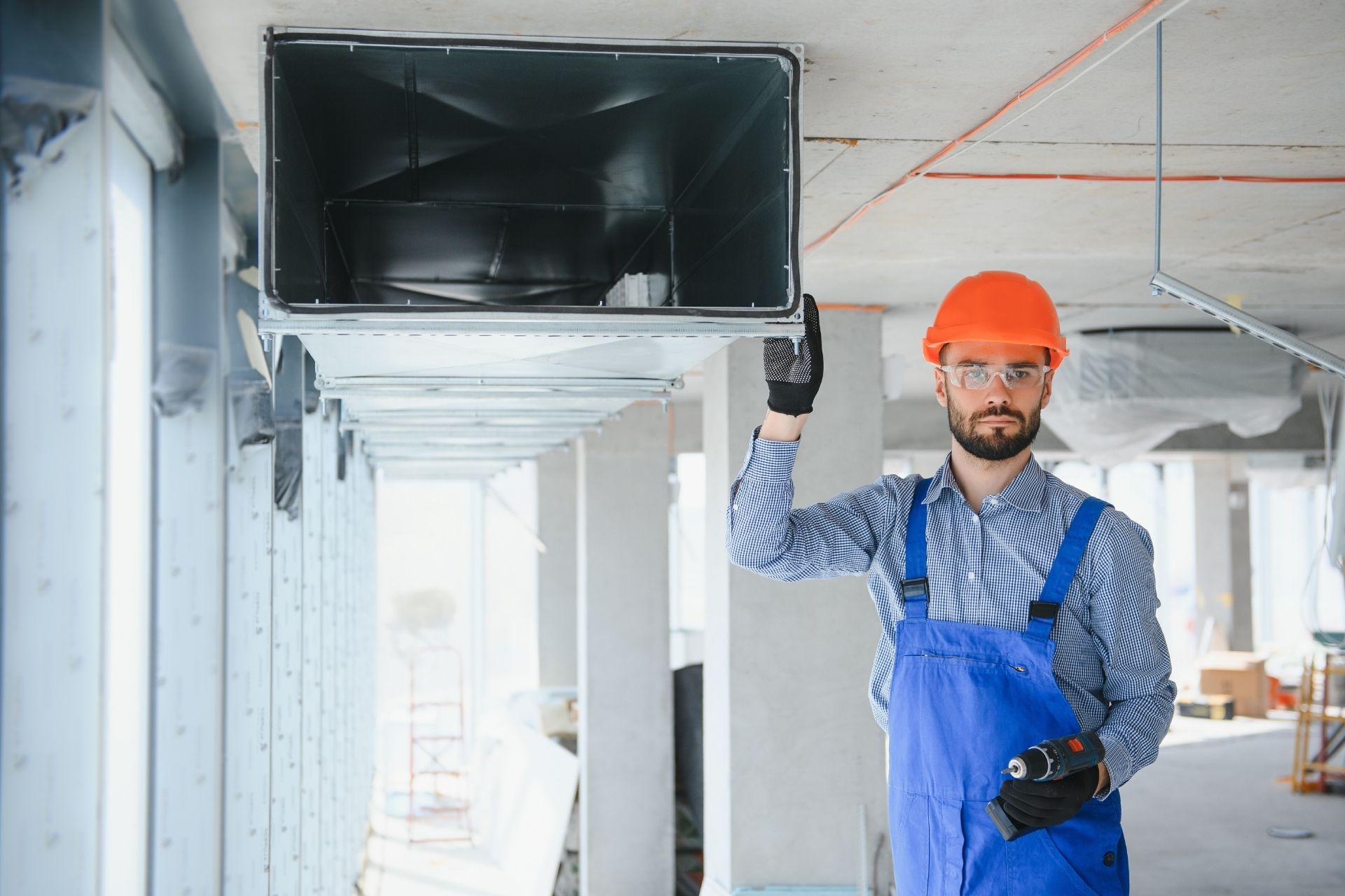HVAC technician wearing mask and hard hat, working on AC units on a rooftop.