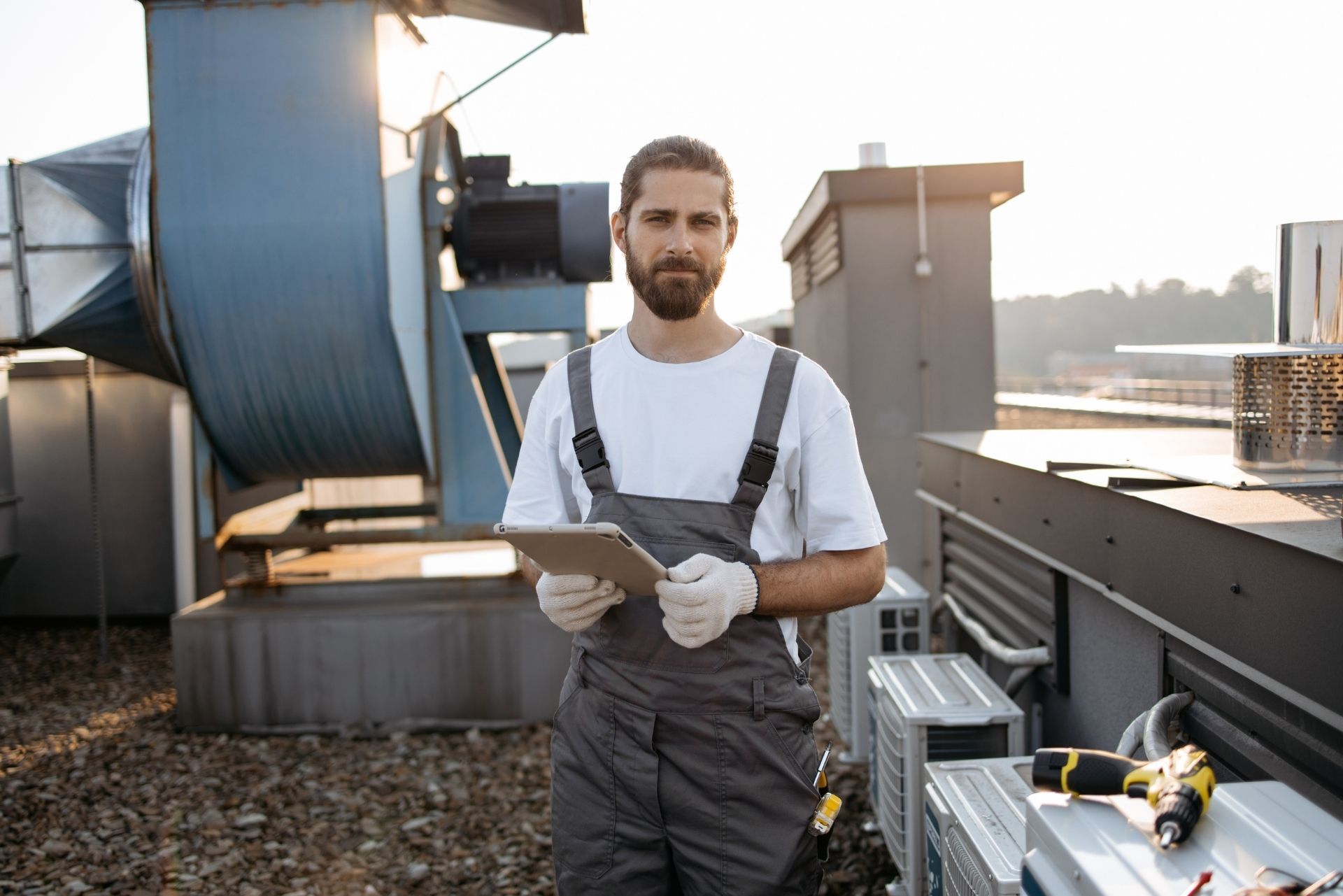 HVAC technician wearing mask and hard hat, working on AC units on a rooftop.