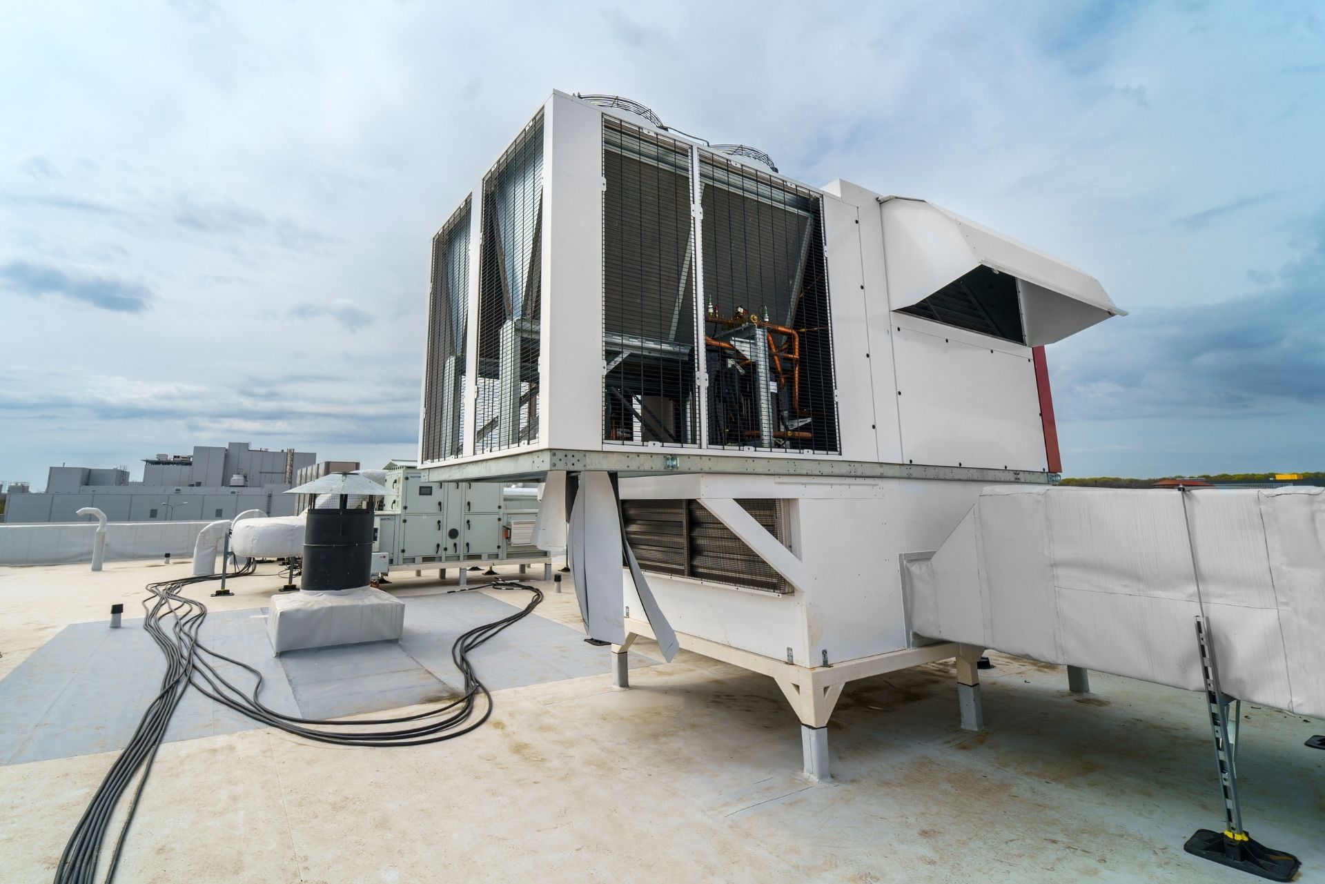 HVAC technician wearing mask and hard hat, working on AC units on a rooftop.