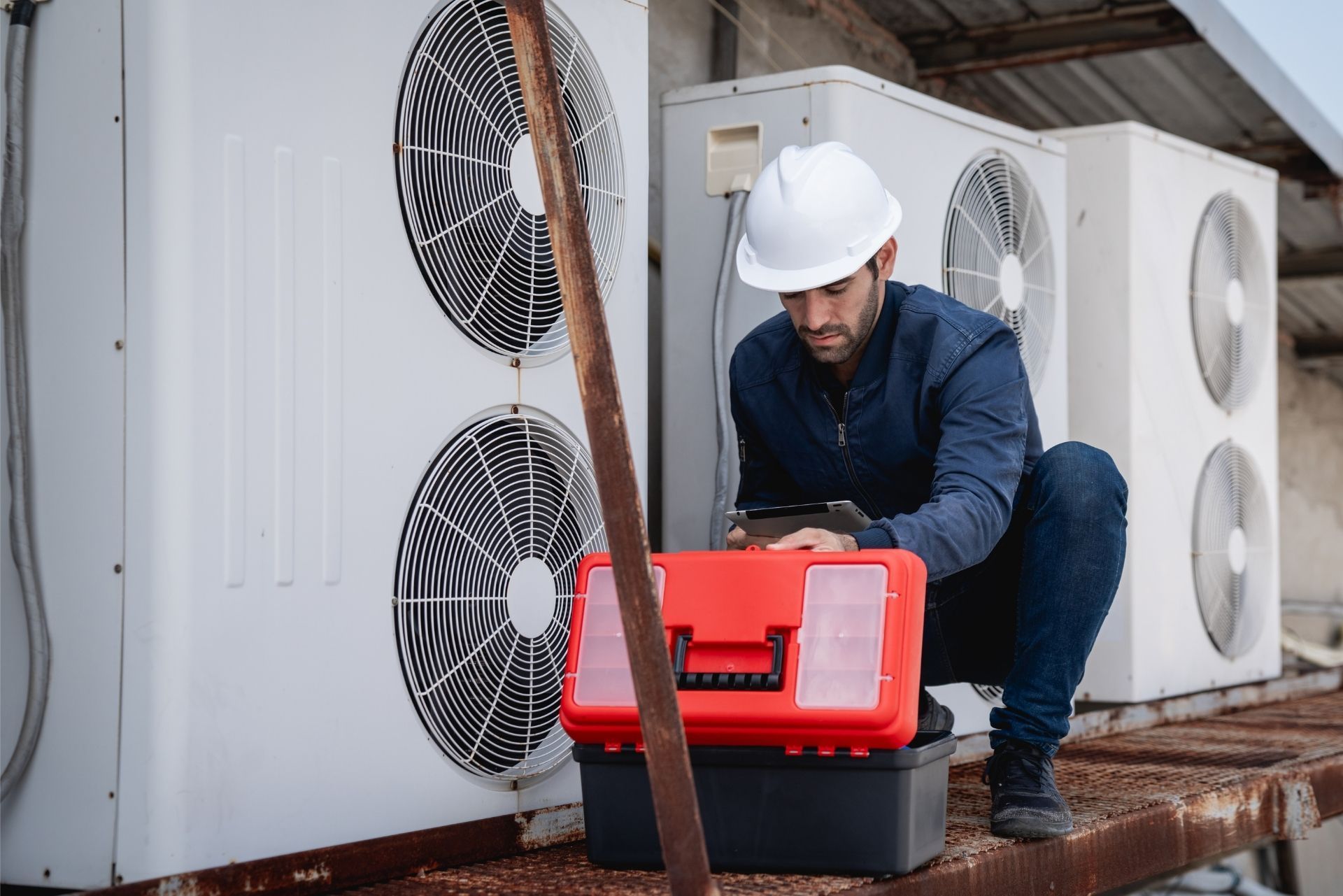HVAC technician wearing mask and hard hat, working on AC units on a rooftop. HVAC technician wearing mask and hard hat, working on AC units on a rooftop.