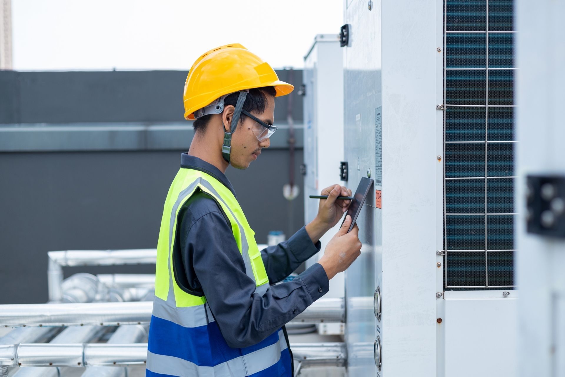 HVAC technician wearing mask and hard hat, working on AC units on a rooftop.