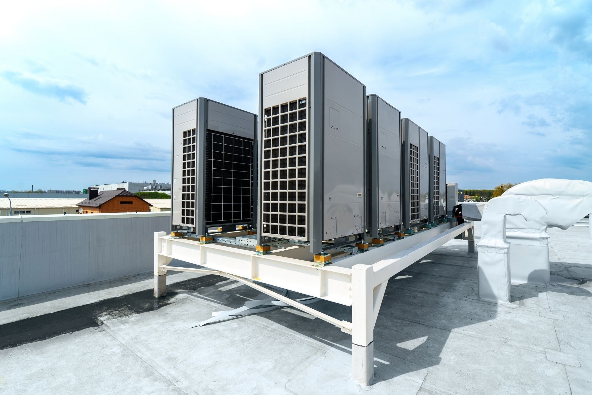 HVAC technician wearing mask and hard hat, working on AC units on a rooftop.