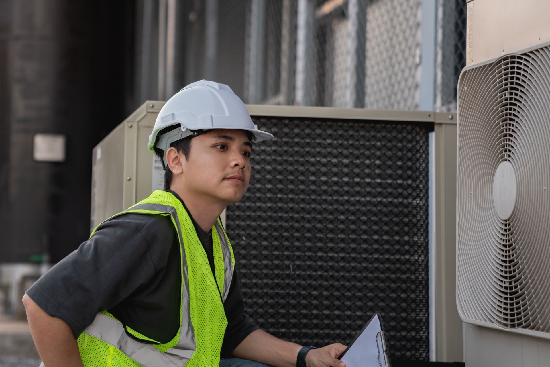 HVAC technician wearing mask and hard hat, working on AC units on a rooftop.