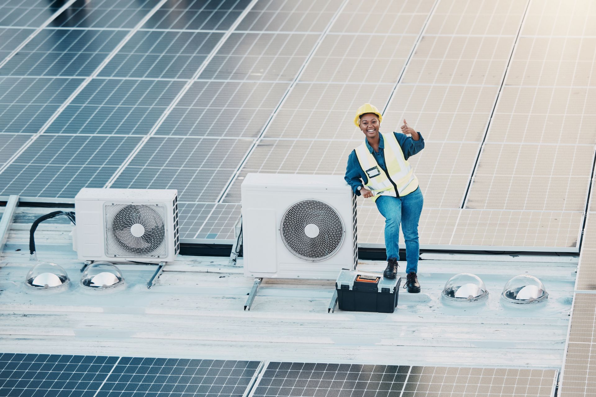 HVAC technician wearing mask and hard hat, working on AC units on a rooftop.