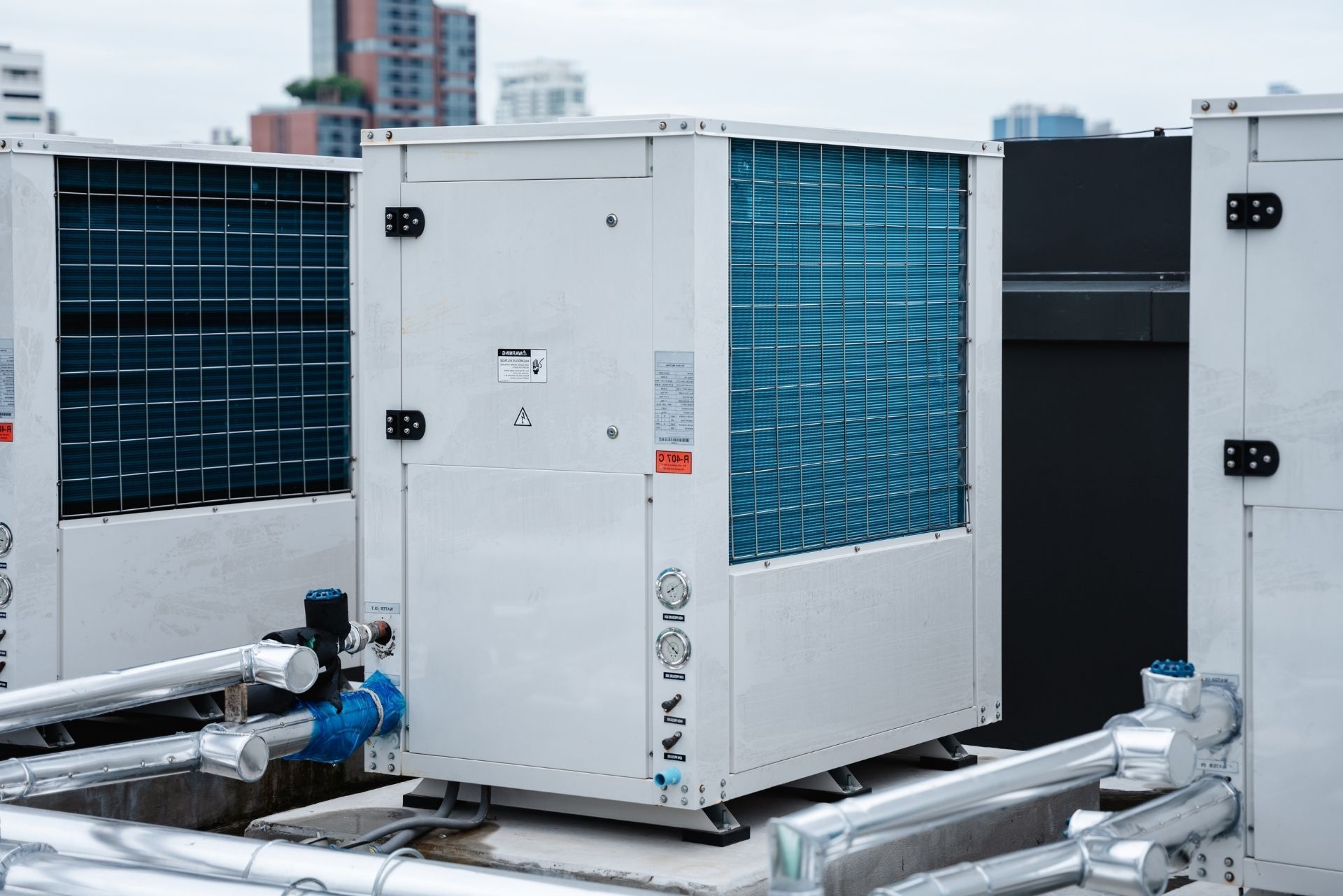 HVAC technician wearing mask and hard hat, working on AC units on a rooftop.