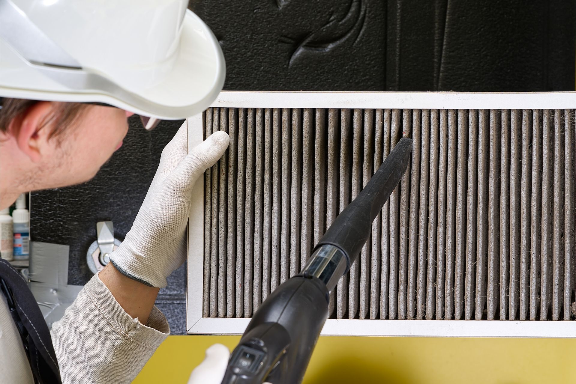 HVAC technician wearing mask and hard hat, working on AC units on a rooftop.