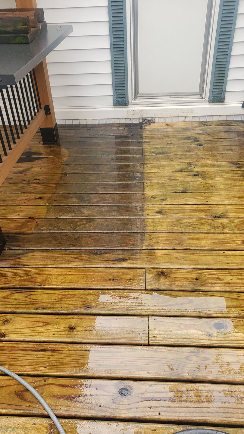 Wooden deck being pressure washed, revealing clean, bright wood next to dirty wood.