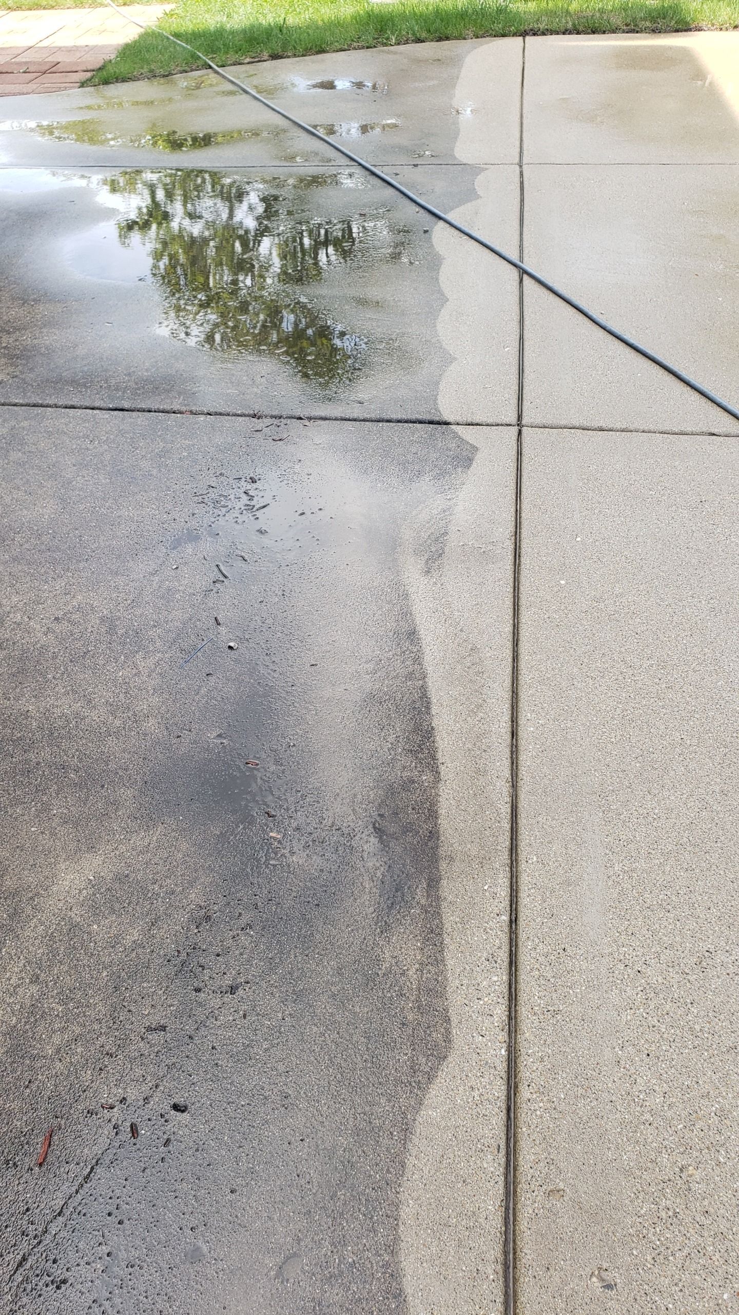 Half of a concrete driveway has been cleaned, showing the difference in color and cleanliness.