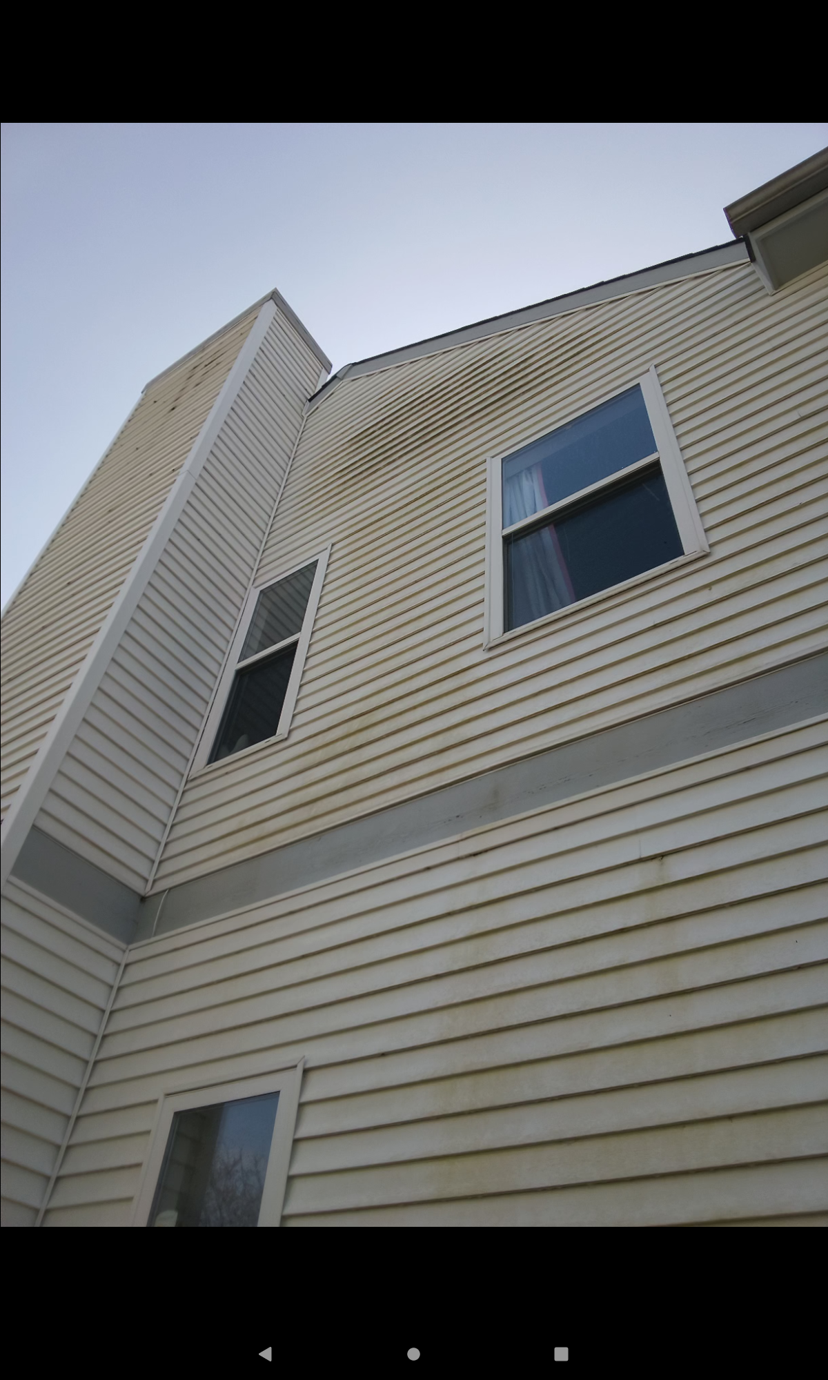 Exterior of a two-story house with dirty white siding, chimney, and windows.