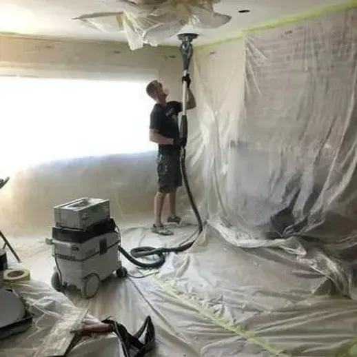 A man is using a tool to remove popcorn ceiling.