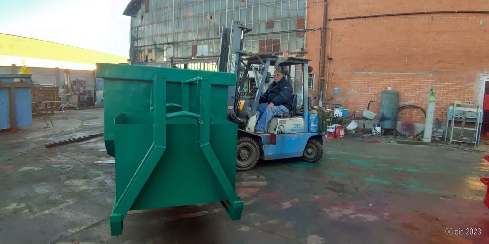 Un uomo sta guidando un carrello elevatore accanto a un cassonetto verde.