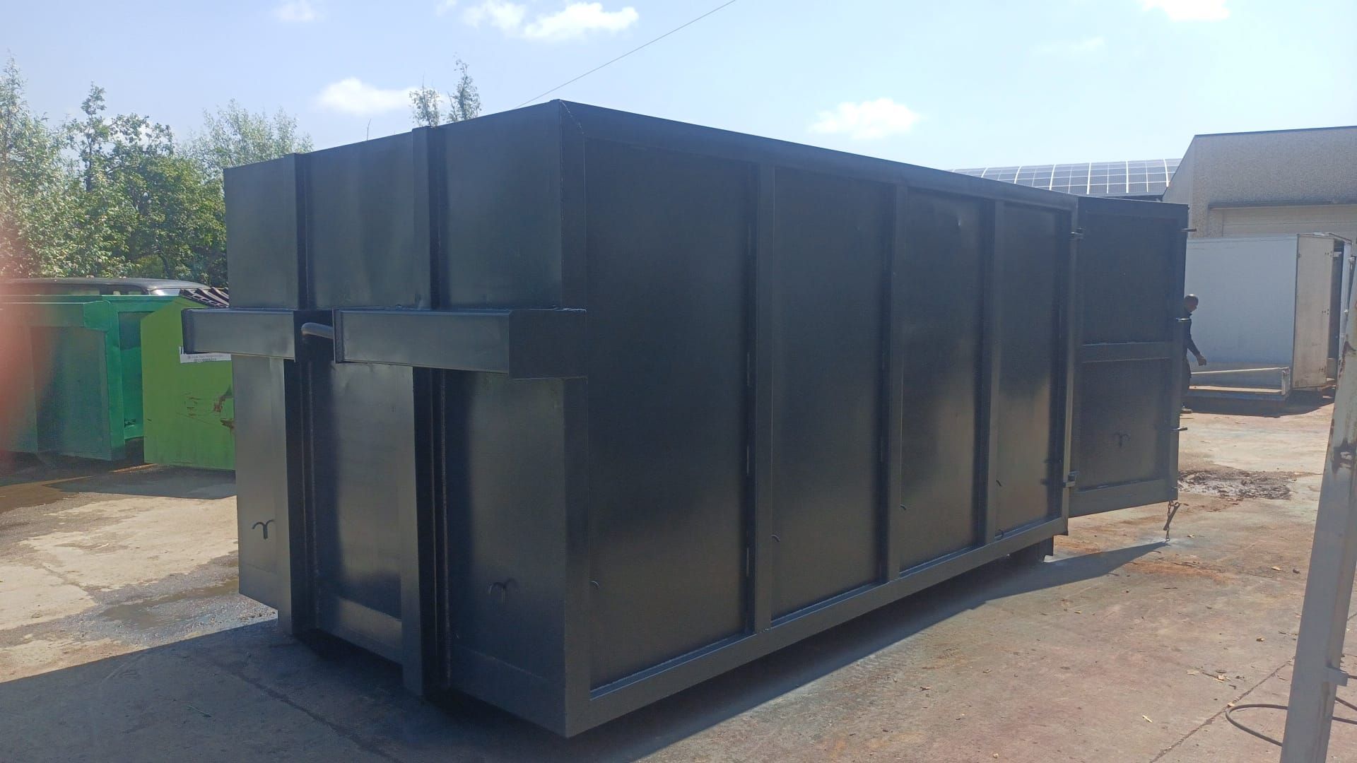 Un grande cassonetto nero è appoggiato a terra in un parcheggio.