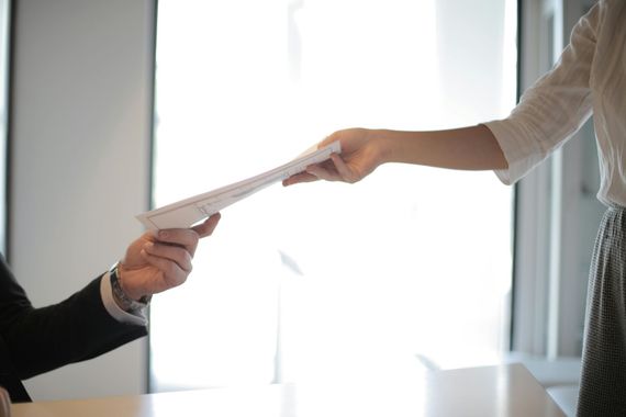 Two people exchange a document across a bright office desk