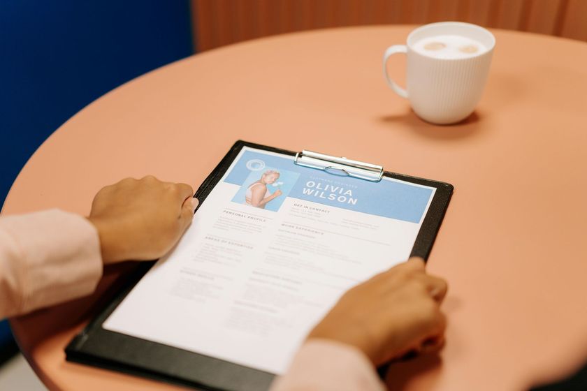Hands using a tablet on a round pink table beside a white coffee cup.