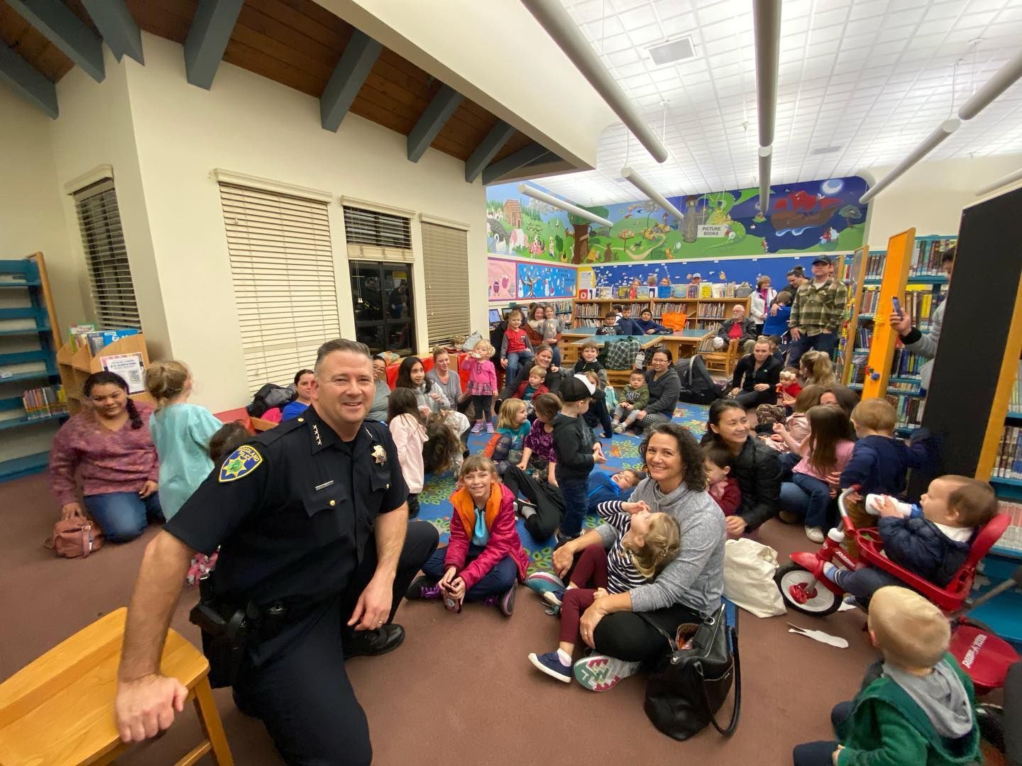 A group of people and children sitting with a police officer posed for a photograph in a library