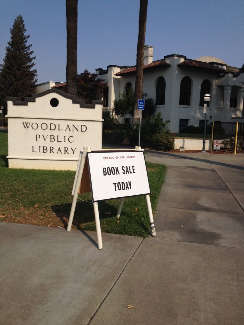 A sign for the woodland public library says book sale today