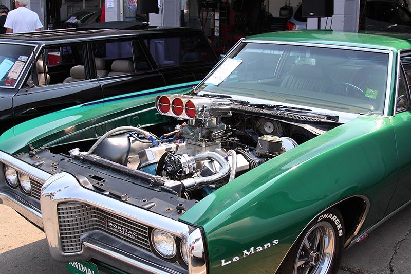 A green muscle car with the hood open is parked in front of a garage.
