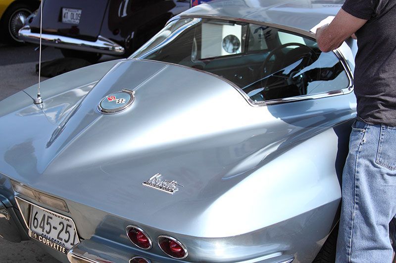 A man is opening the hood of a silver corvette.