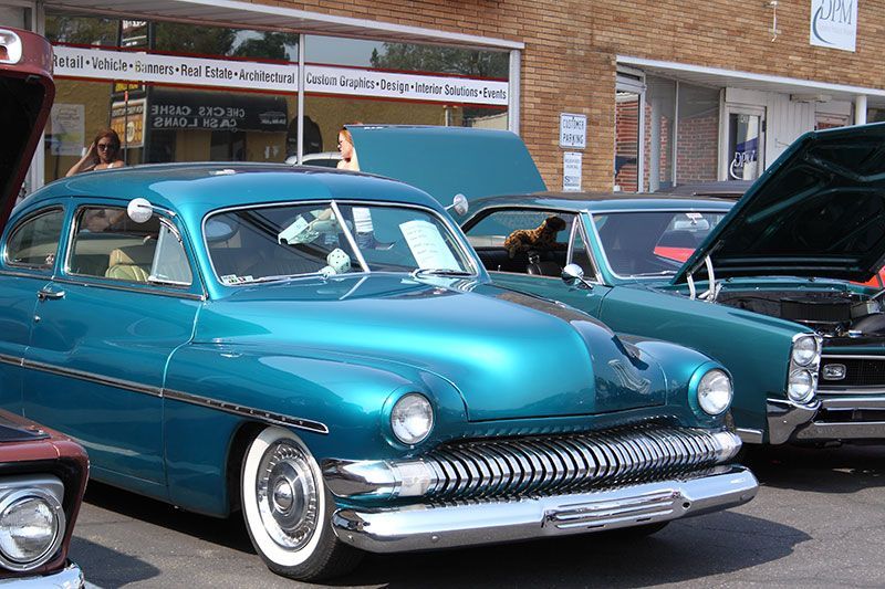A blue car is parked in front of a building with the hood up.