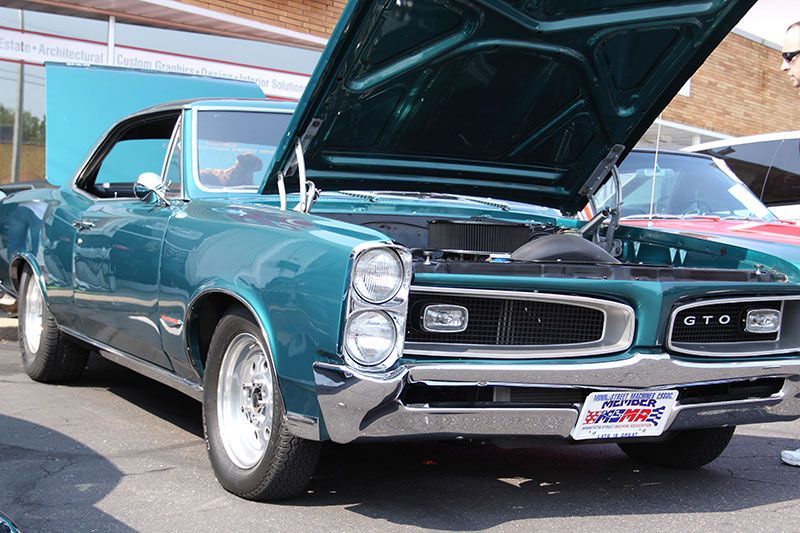 A blue car with the hood up is parked in a parking lot.