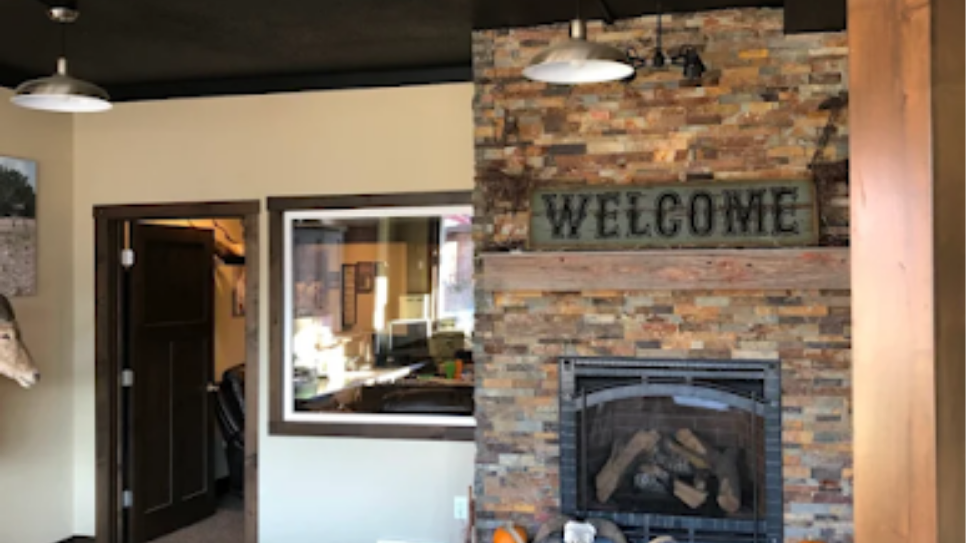Interior room with brick fireplace and “WELCOME” sign, black pendant lights, and a wall mirror.