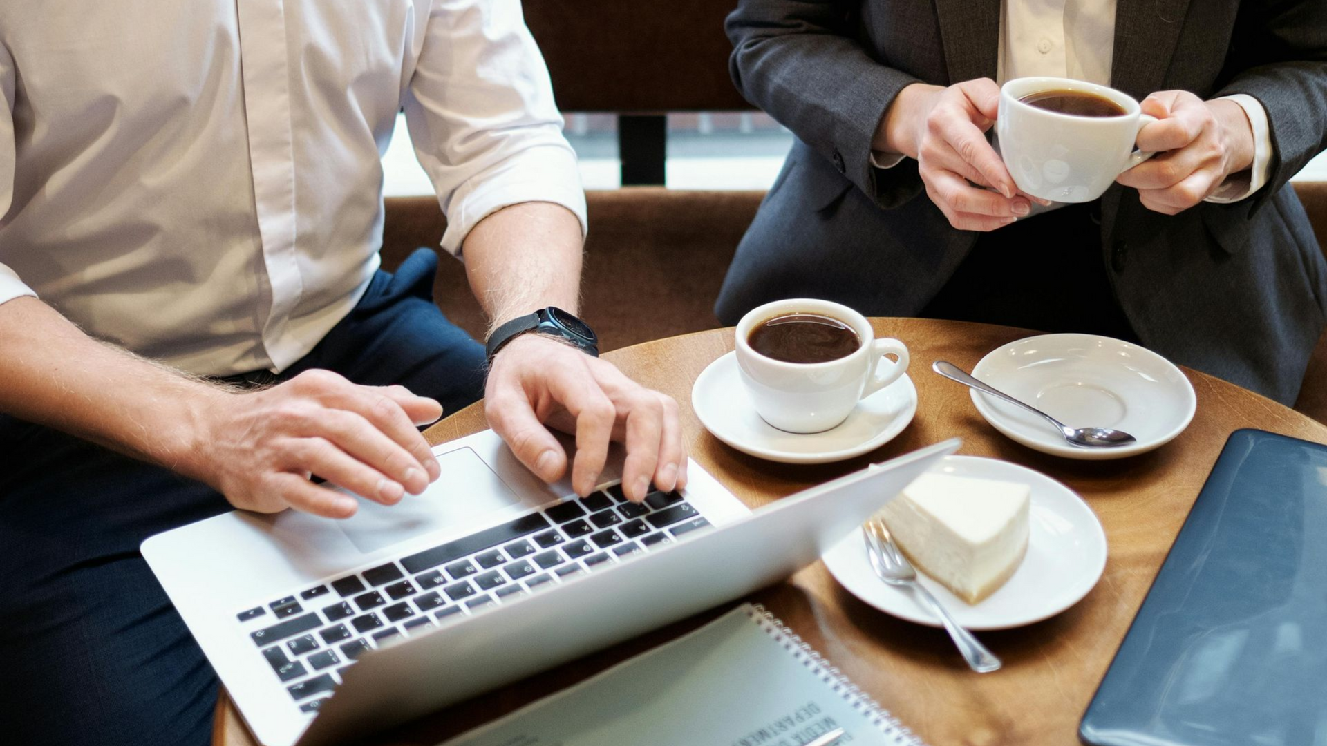 People at a table with a laptop and coffee cups in a café meeting.