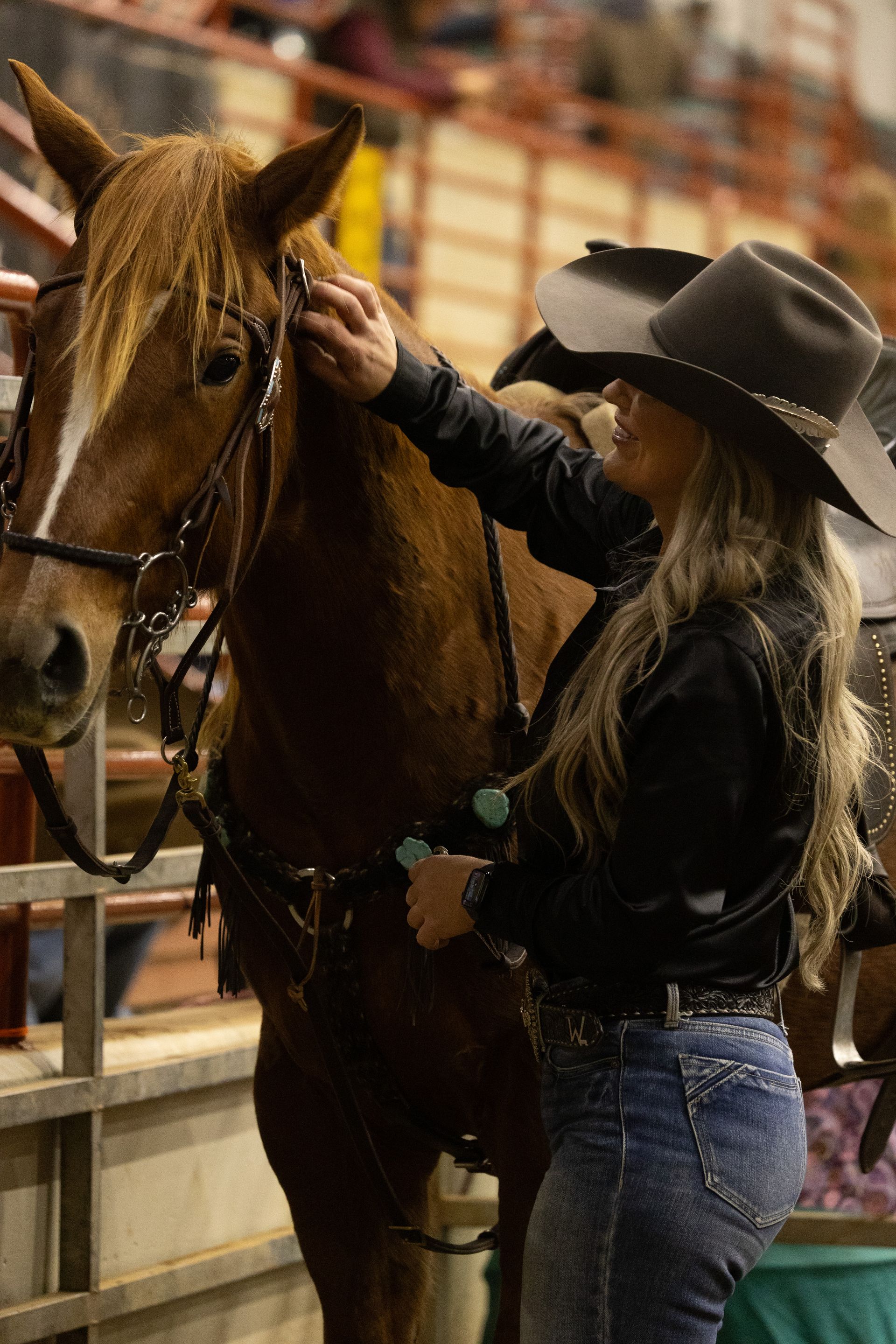 A woman in a cowboy hat is petting a brown horse.