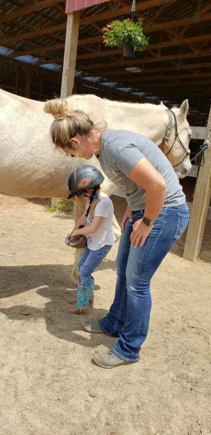 A woman and a little girl are standing next to a horse in a stable.