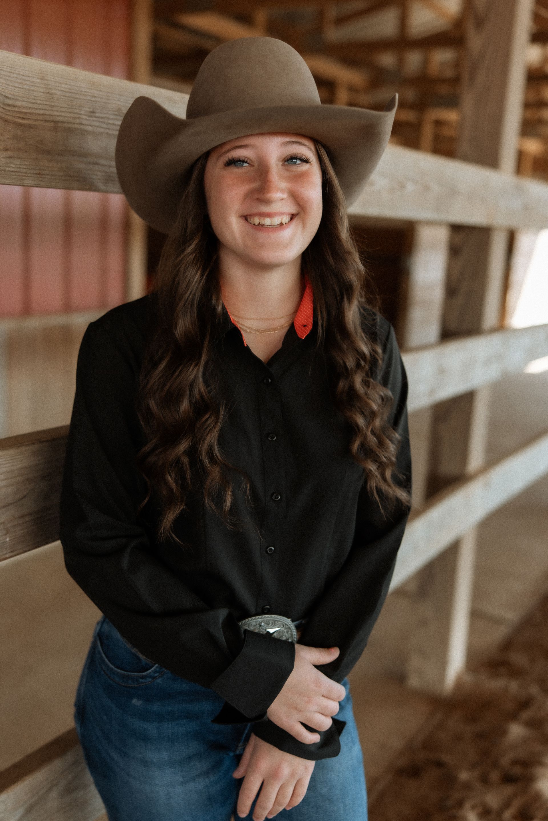 A woman wearing a cowboy hat and a black shirt is standing next to a wooden fence.