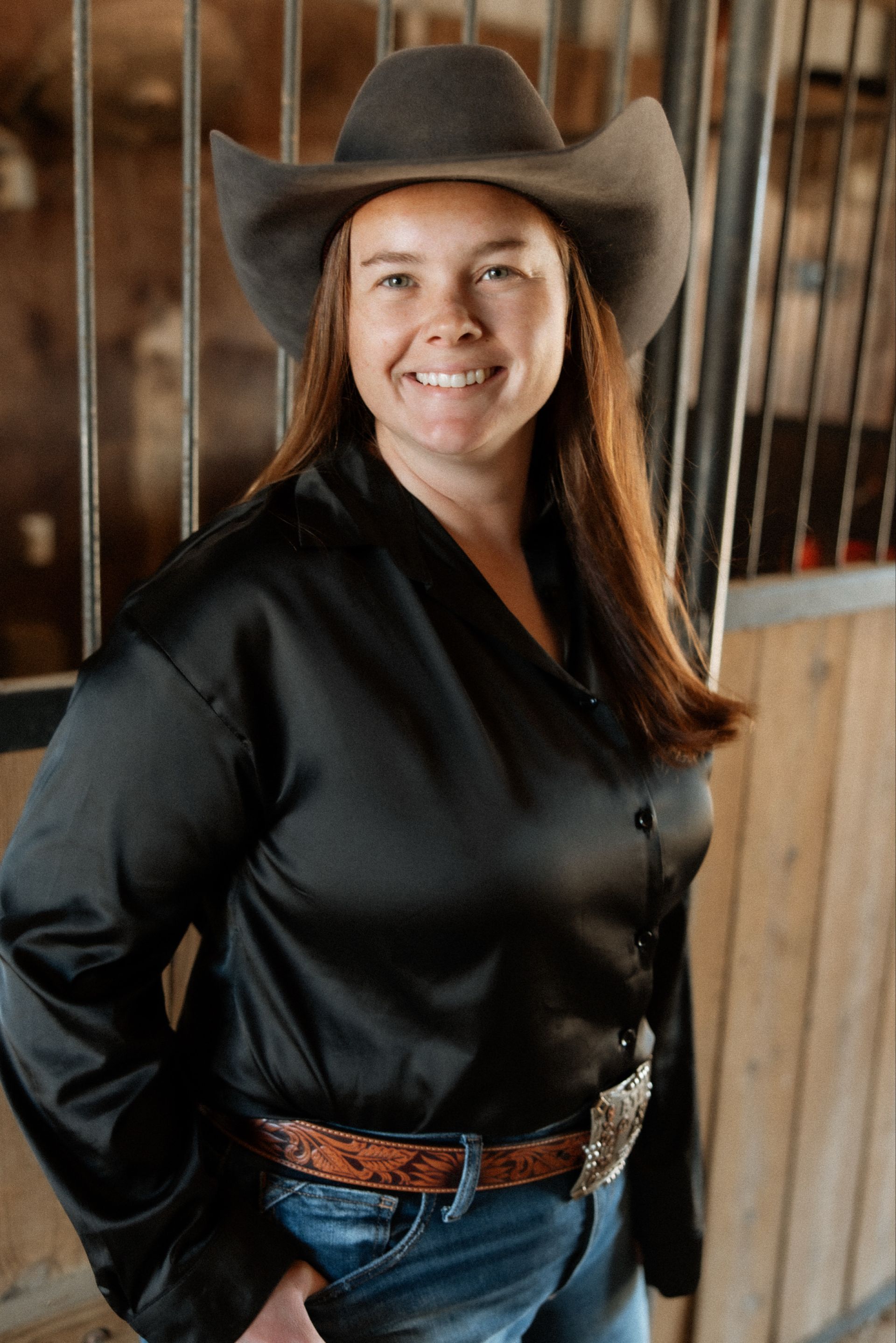 A woman wearing a cowboy hat and a black shirt is standing in a barn.