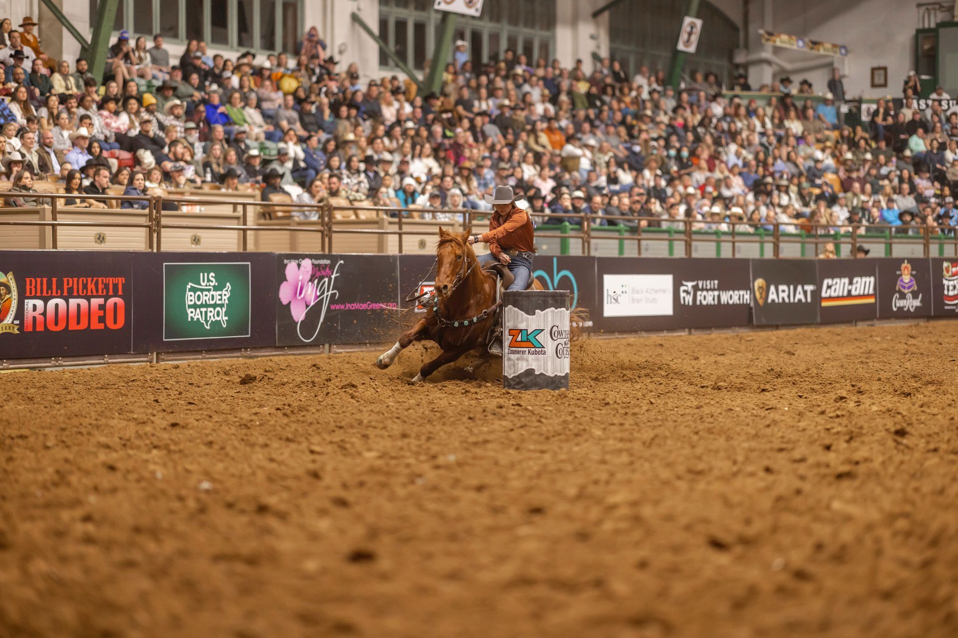 A man is riding a horse around a barrel at a rodeo.