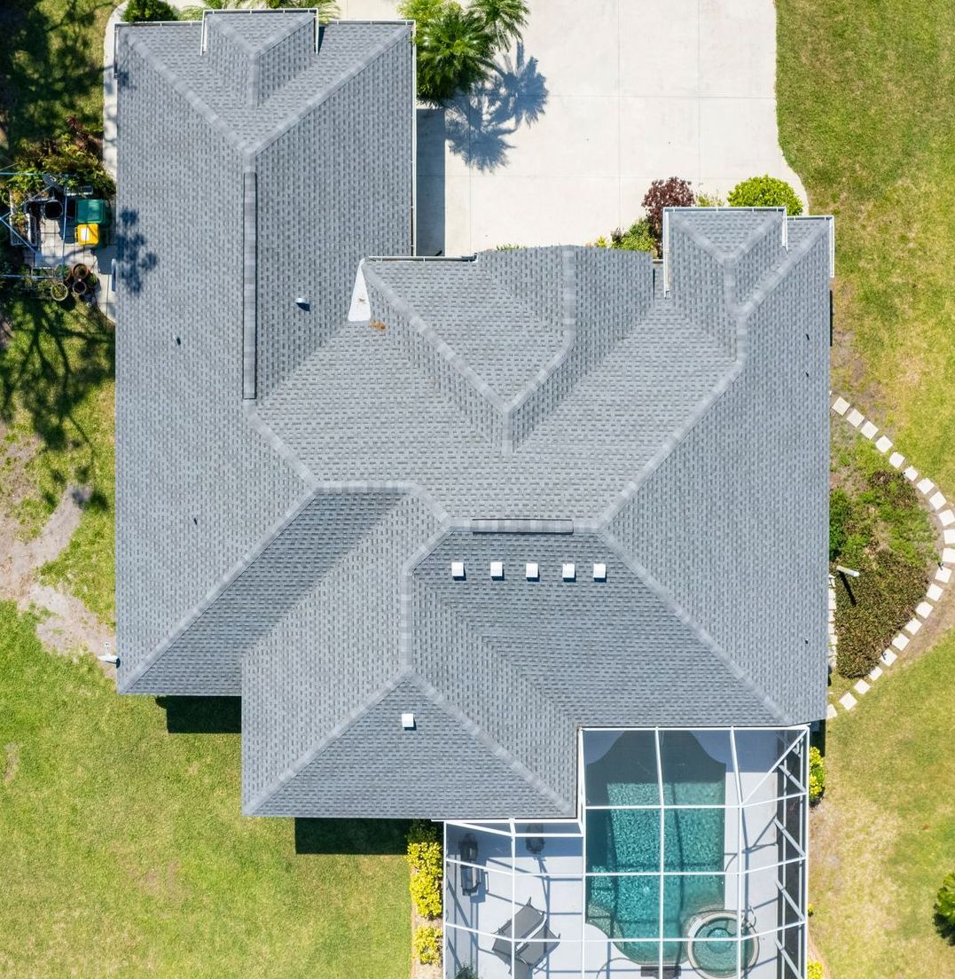 Overhead view of a house with a gray roof, a pool, and green lawn.
