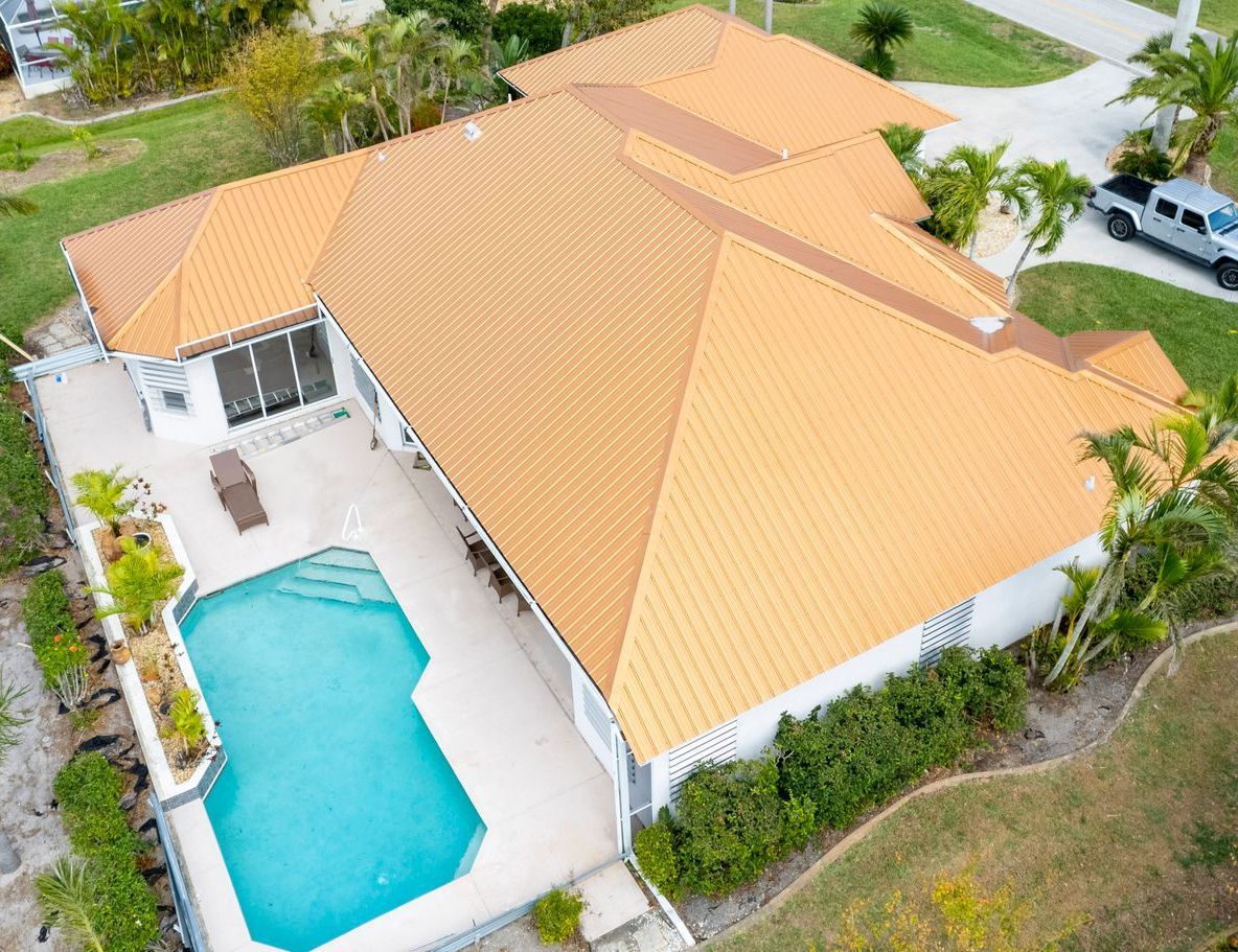 Aerial view of a house with a gold metal roof, pool, and parked truck in the yard.