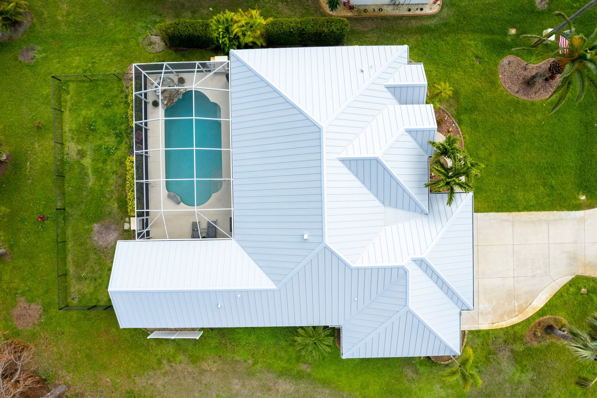 Overhead view of a house with a pool. Green lawn surrounds a light-colored roof and a screened pool.