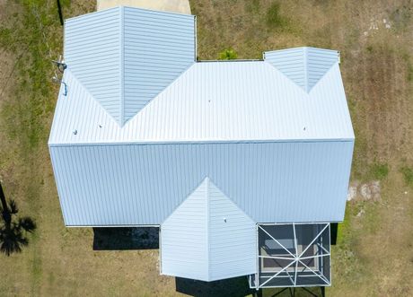 Aerial view of a house with a light-colored roof.  The roof has multiple gabled sections.