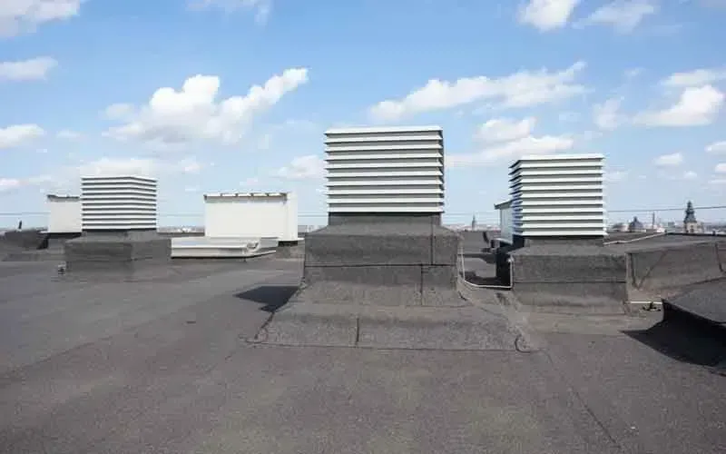 Flat rooftop with several square ventilation units against a blue sky with fluffy white clouds.