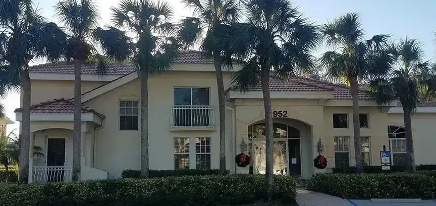 A beige building with a red-tiled roof, palm trees, and a balcony.