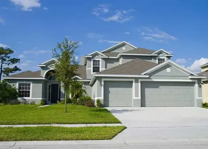 Two-story gray house with a green lawn and blue sky. Two-car garage visible.