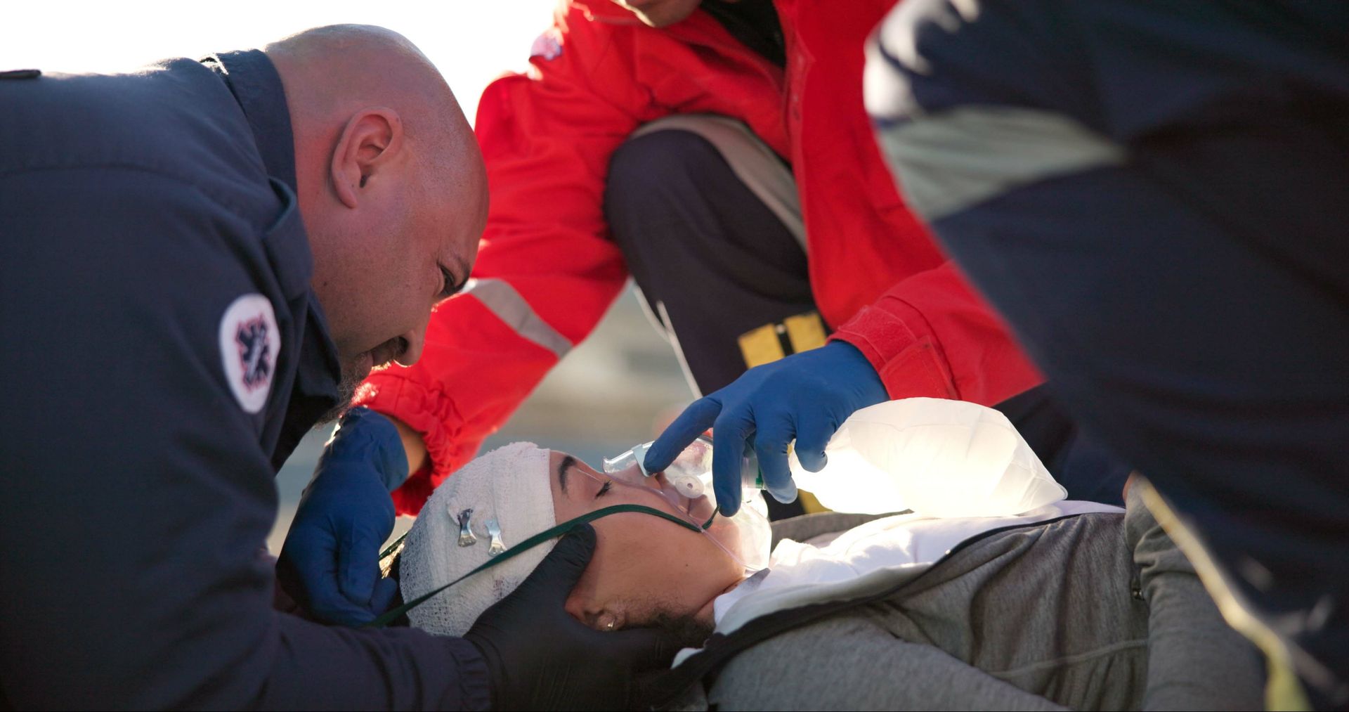Emergency medical personnel tending to a person on a stretcher; oxygen mask in place.