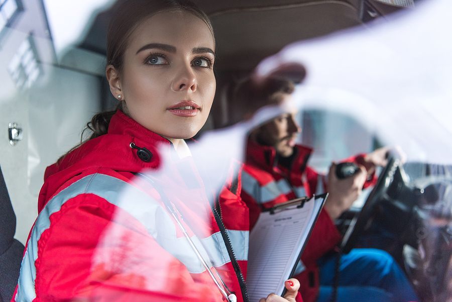 Emergency medical technician in red jacket holding clipboard in ambulance, looking concerned.