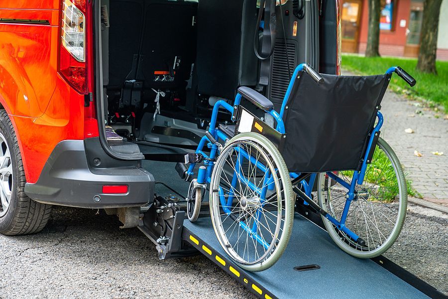 Wheelchair on ramp of accessible orange van. Black seat, blue wheels, outdoor setting.