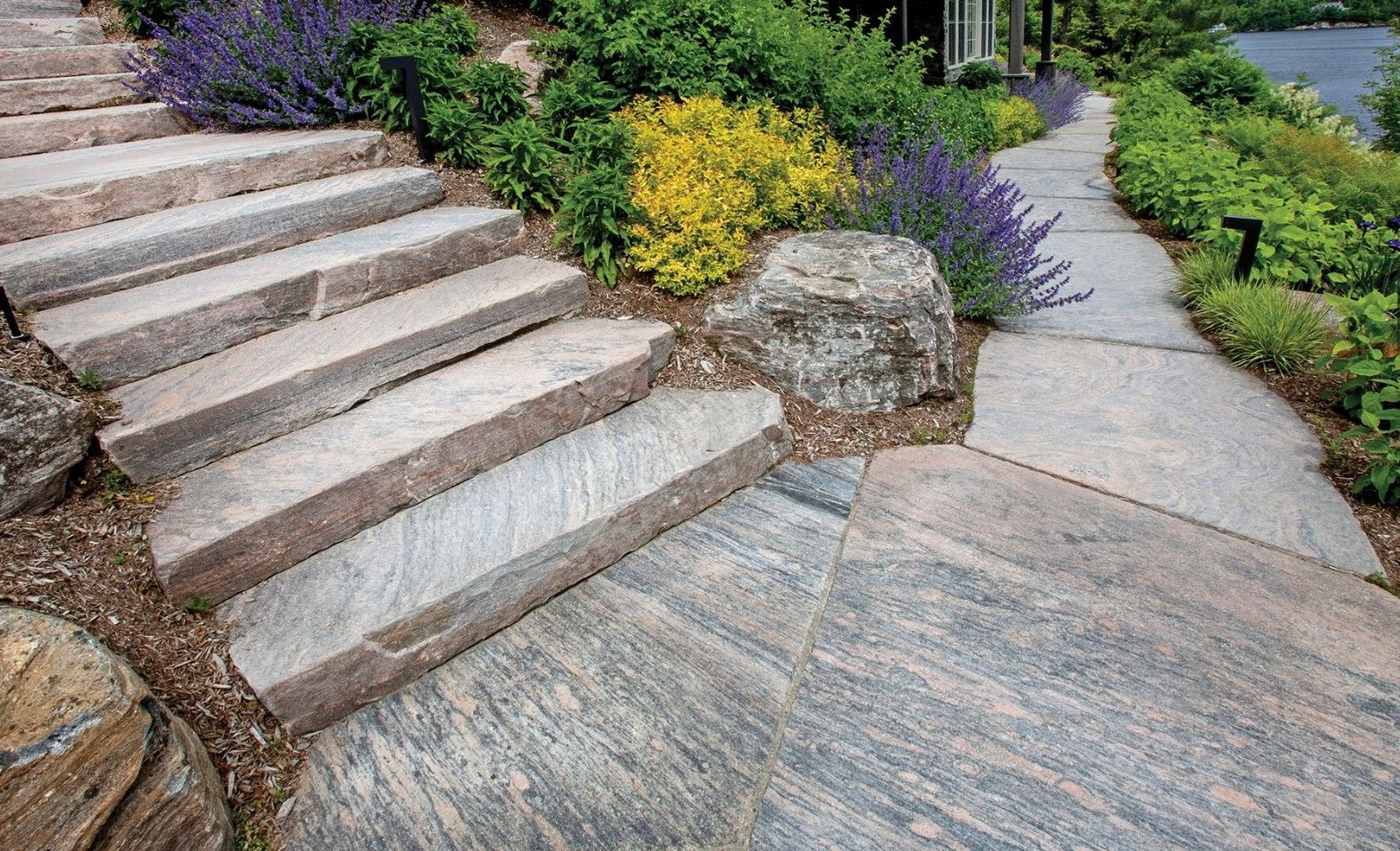 A stone walkway with stairs leading up to a lush green garden.