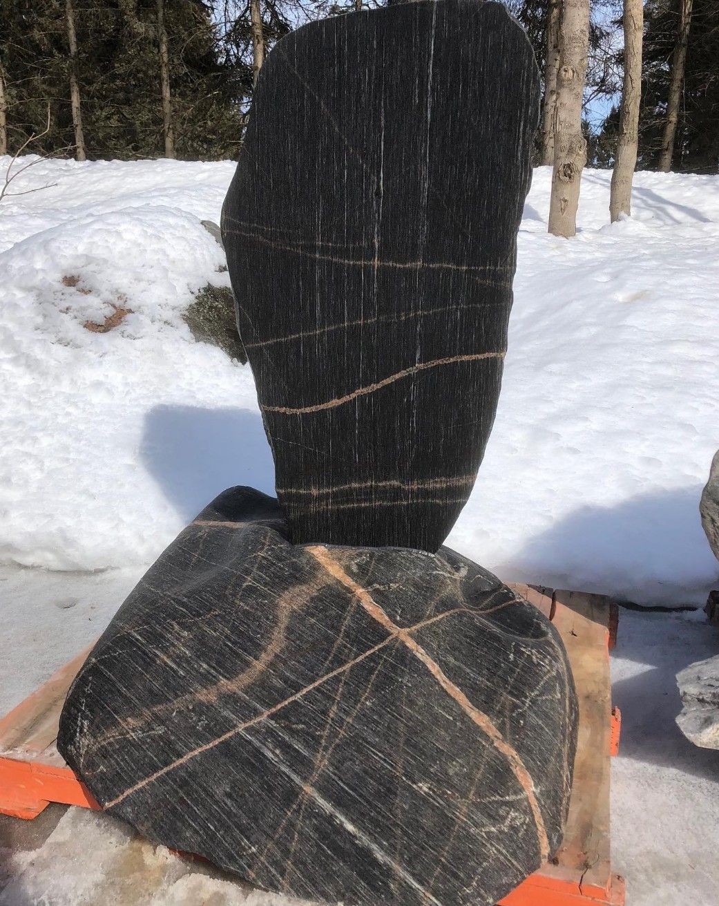 A large black rock is sitting in the snow.