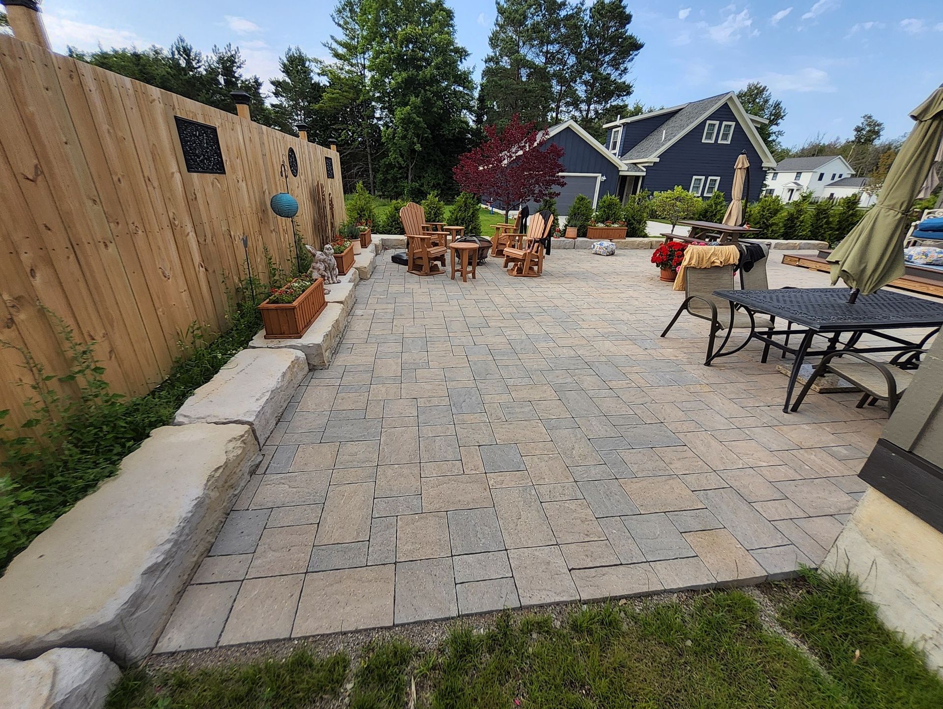 A patio with a wooden fence , chairs , tables and umbrellas.