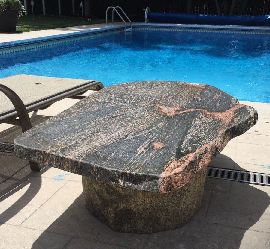 A large stone table sits in front of a swimming pool