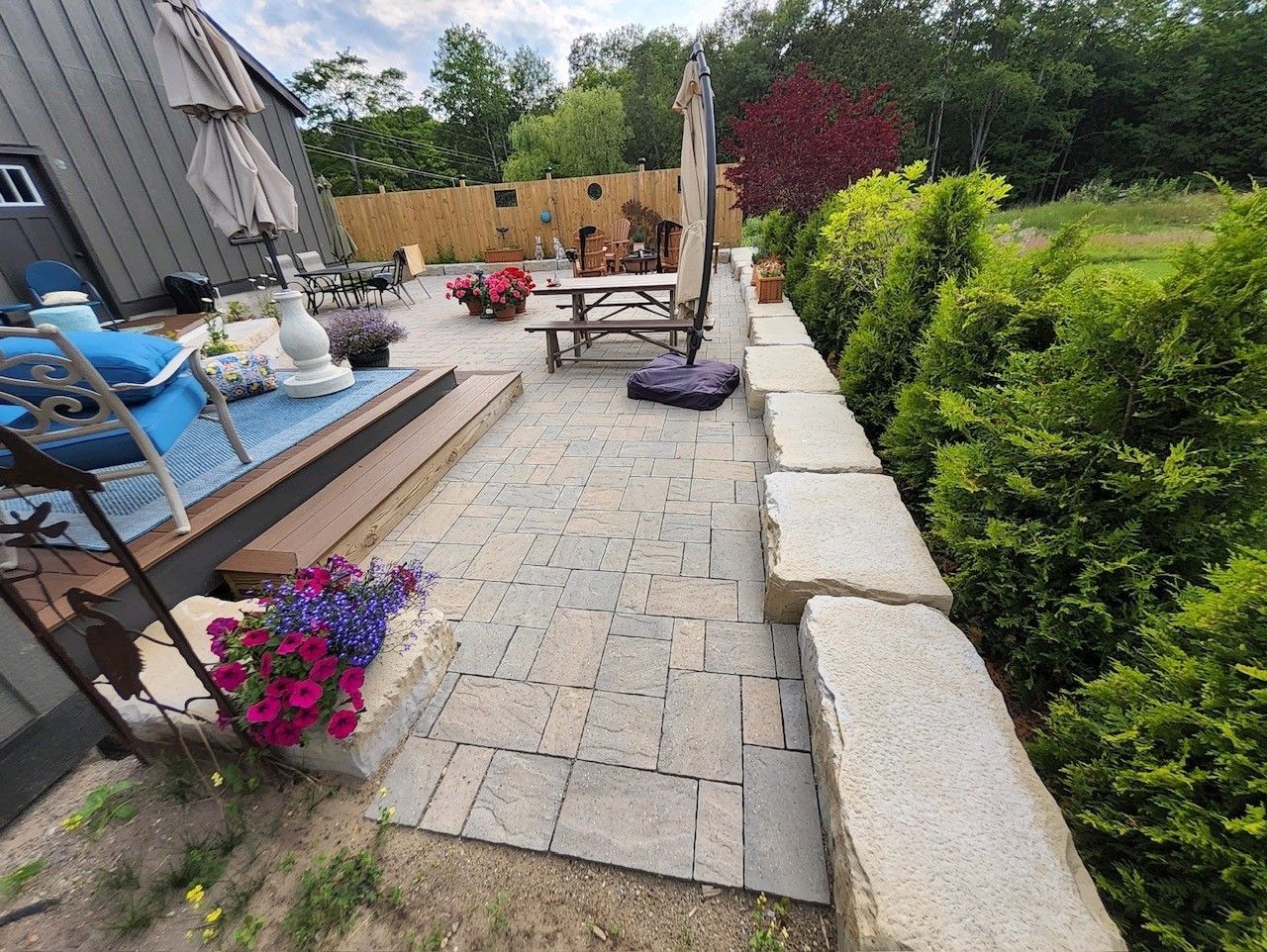 A patio with a picnic table , chairs , umbrellas and flowers.