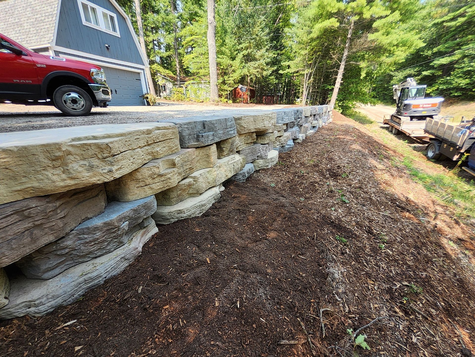 A red truck is parked on the side of a road next to a stone wall.